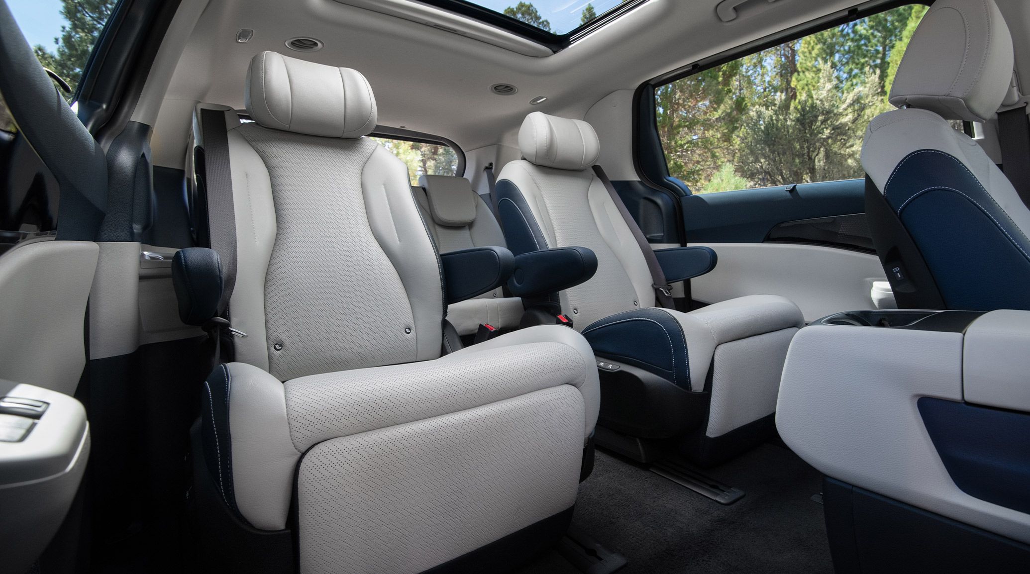 An interior shot of the 2027 Kia Carnival Hybrid in navy and gray featuring spacious second-row captain’s chairs with premium materials, leather seats, and a bright, open cabin.