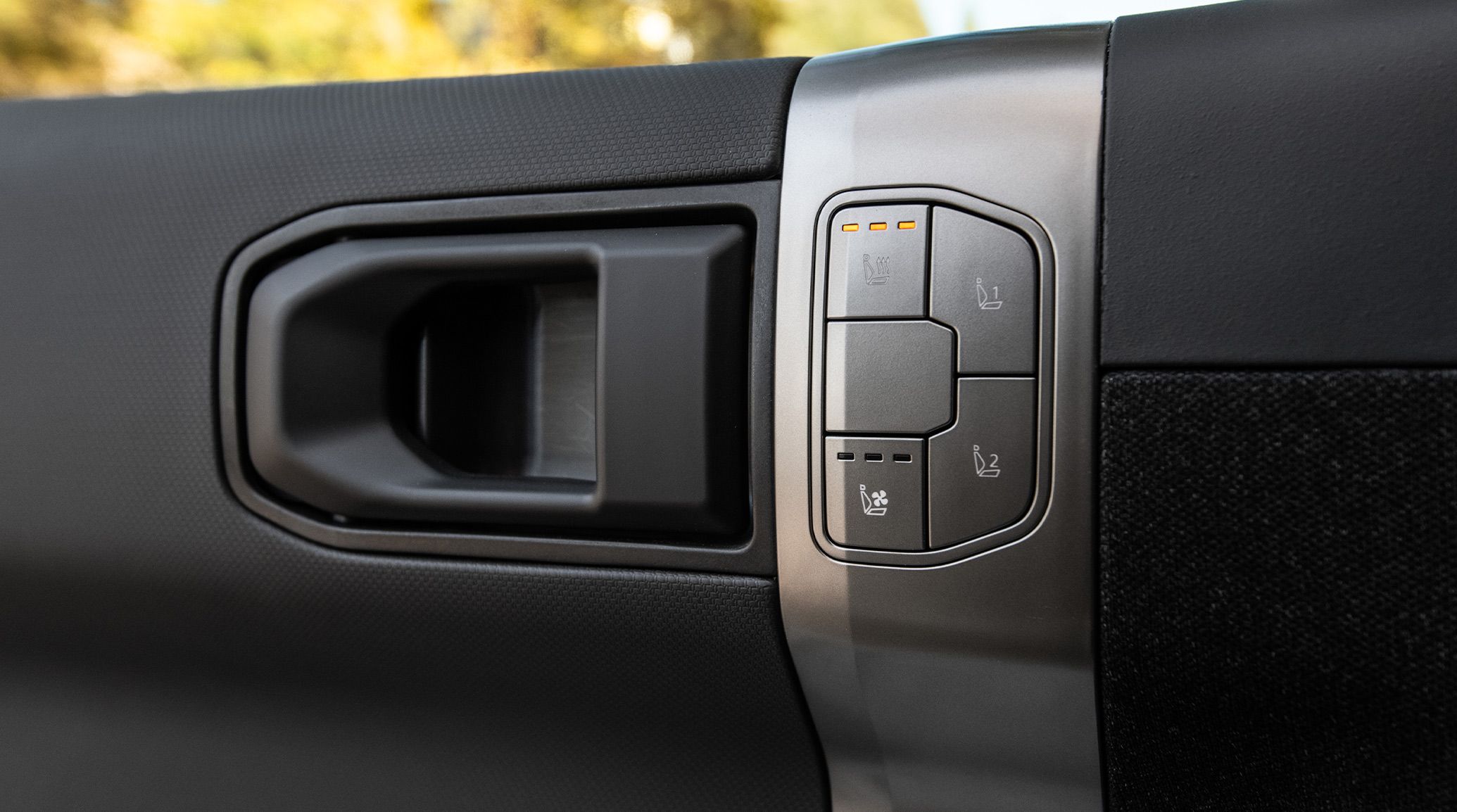 Close-up photograph of a door handle inside the 2027 Kia EV3 compact electric SUV, along with climate control buttons for the front seats.