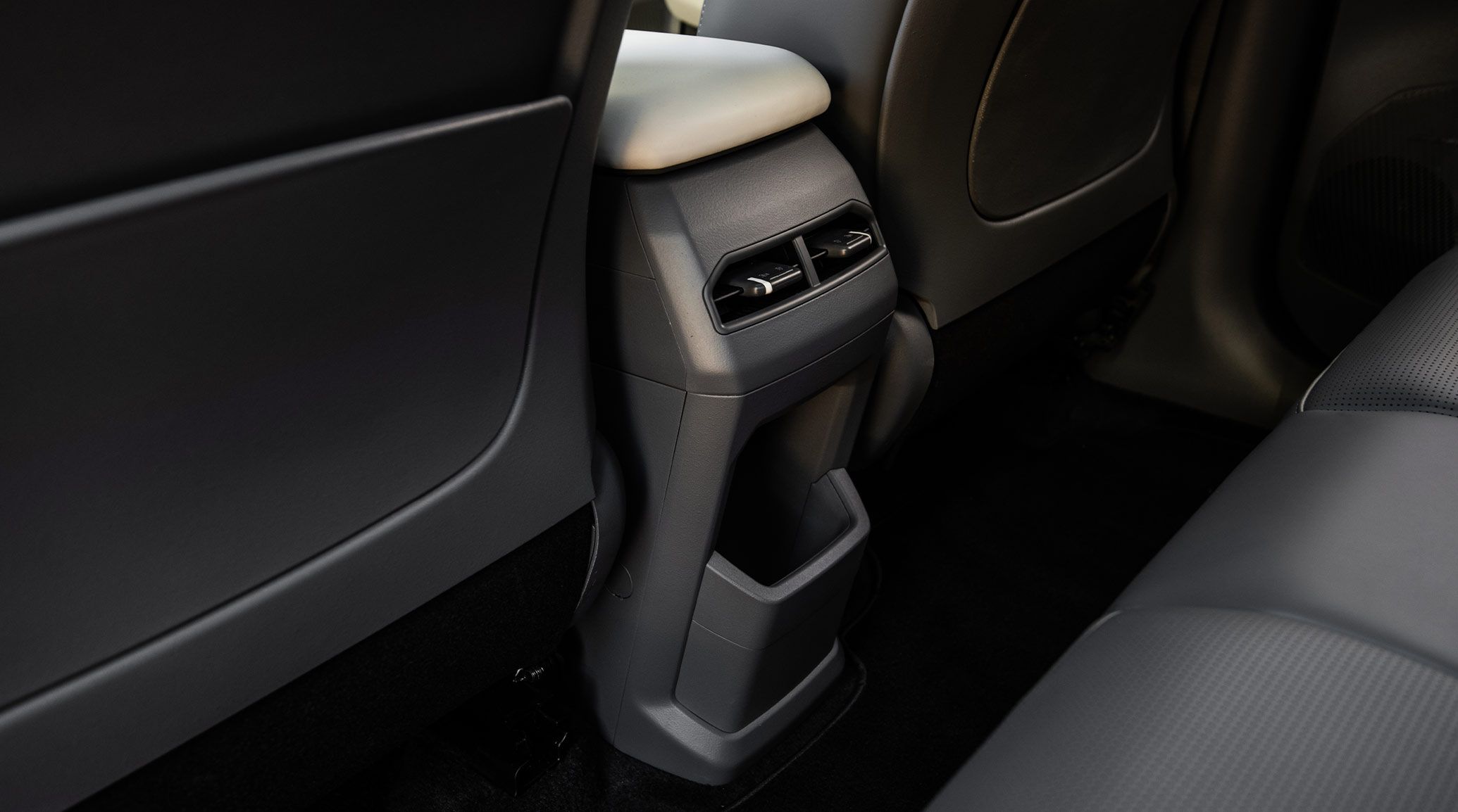 Interior of the 2027 Kia EV3 compact electric SUV from the back seats, showing the back of the center section with climate vents and a large storage pocket.