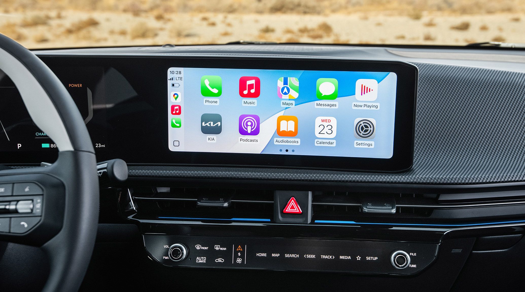 Close-up shot of the center console inside the 2026 Kia EV6, displaying wireless connectivity options compatible with Apple CarPlay and Android Auto, showing apps like Phone, Music, Maps, Messages, Now Playing, the KIA app, and more.