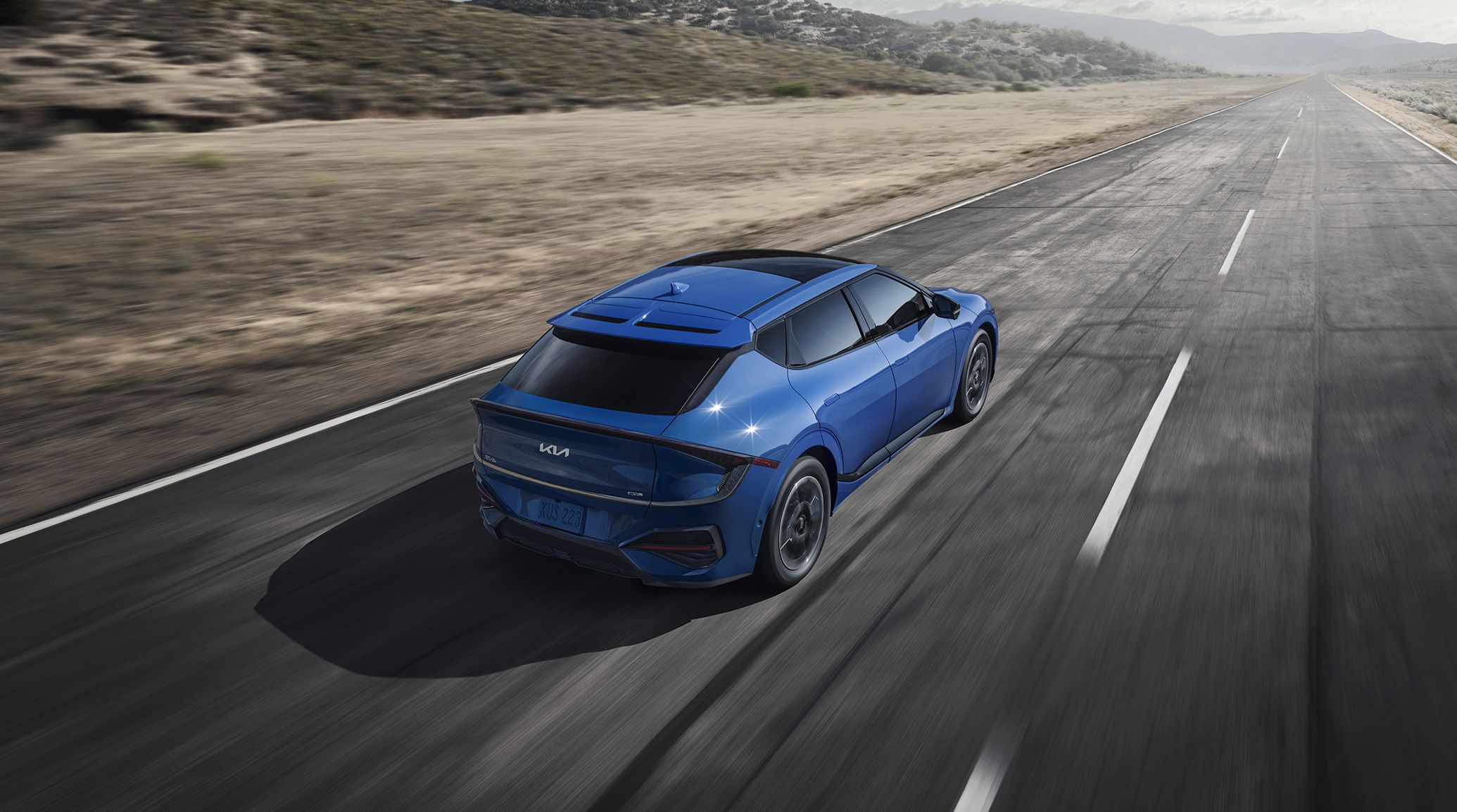 An exciting photograph of the 2026 Kia EV6 electric CUV in blue from above, as it zooms forward on a desert road. The wide sunroof is visible from this angle.