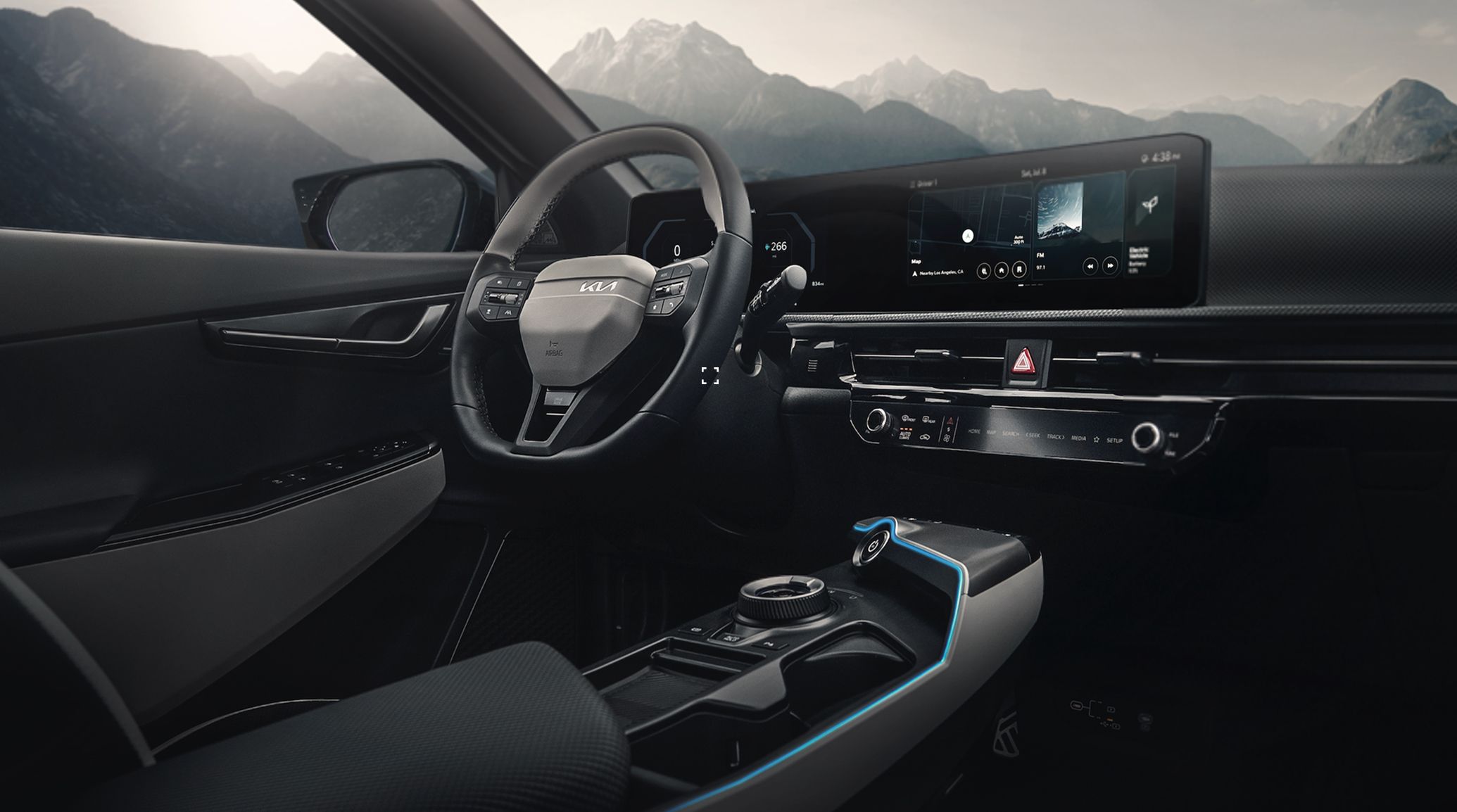 Interior shot of the 2026 Kia EV6 electric CUV showcasing its driver-centric digital cockpit and three-spoke steering wheel, as well as the center console and dashboard digital displays. Towering grey mountains are visible in the hazy sunlight outside the windshield.
