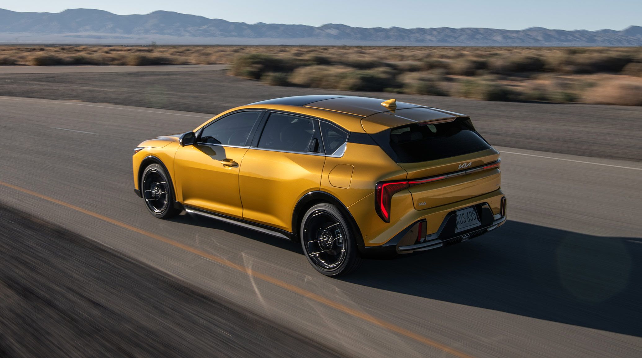 Dynamic Shot of a 2026 K4 Hatchback in Gold Yellow from the back as it is driving through nature, specifically in the desert
