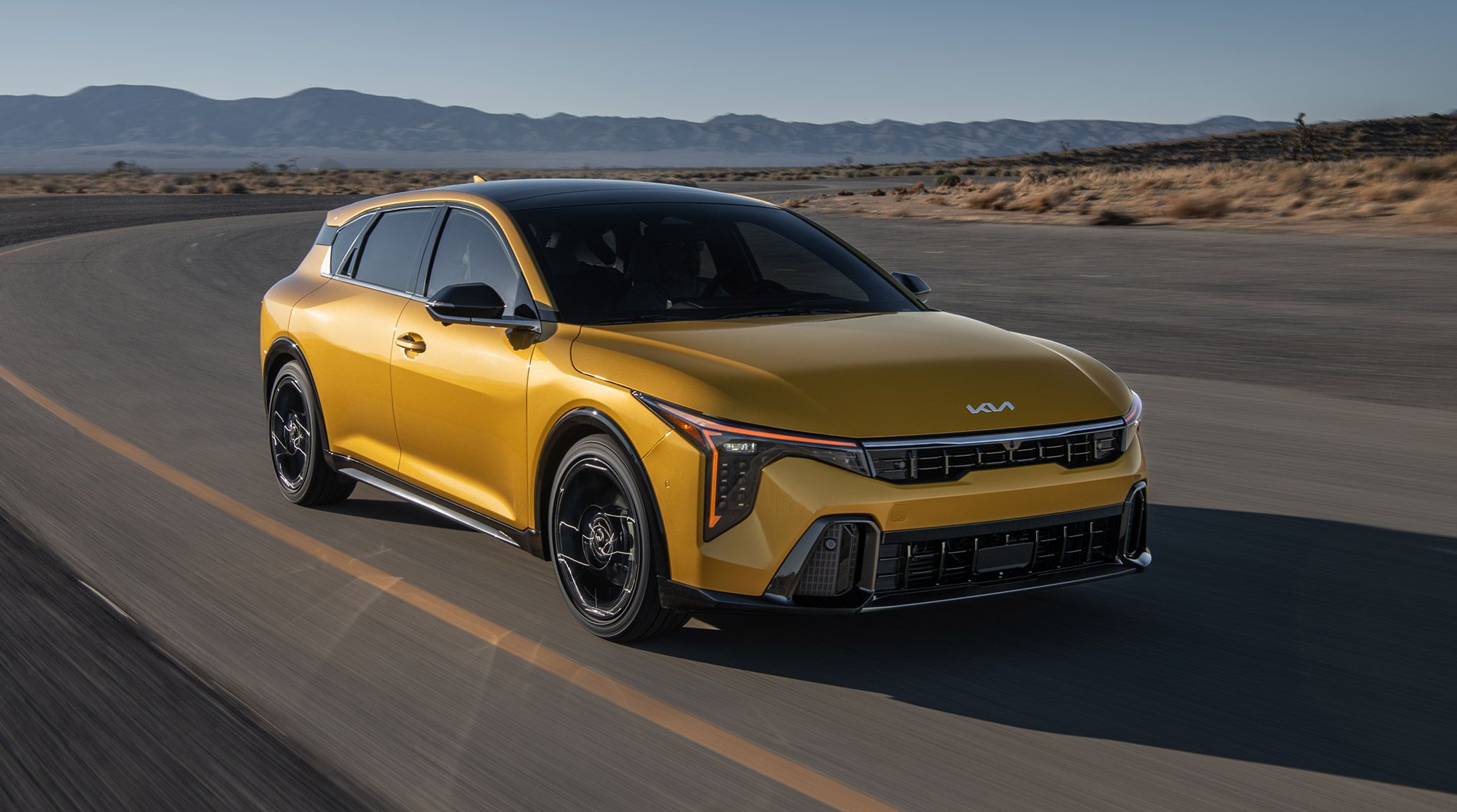 An exterior shot of the 2026 K4 Hatchback GT-Line Turbo driving through the desert, with the shot focusing on it's gloss black side sills and wheel arch molding.