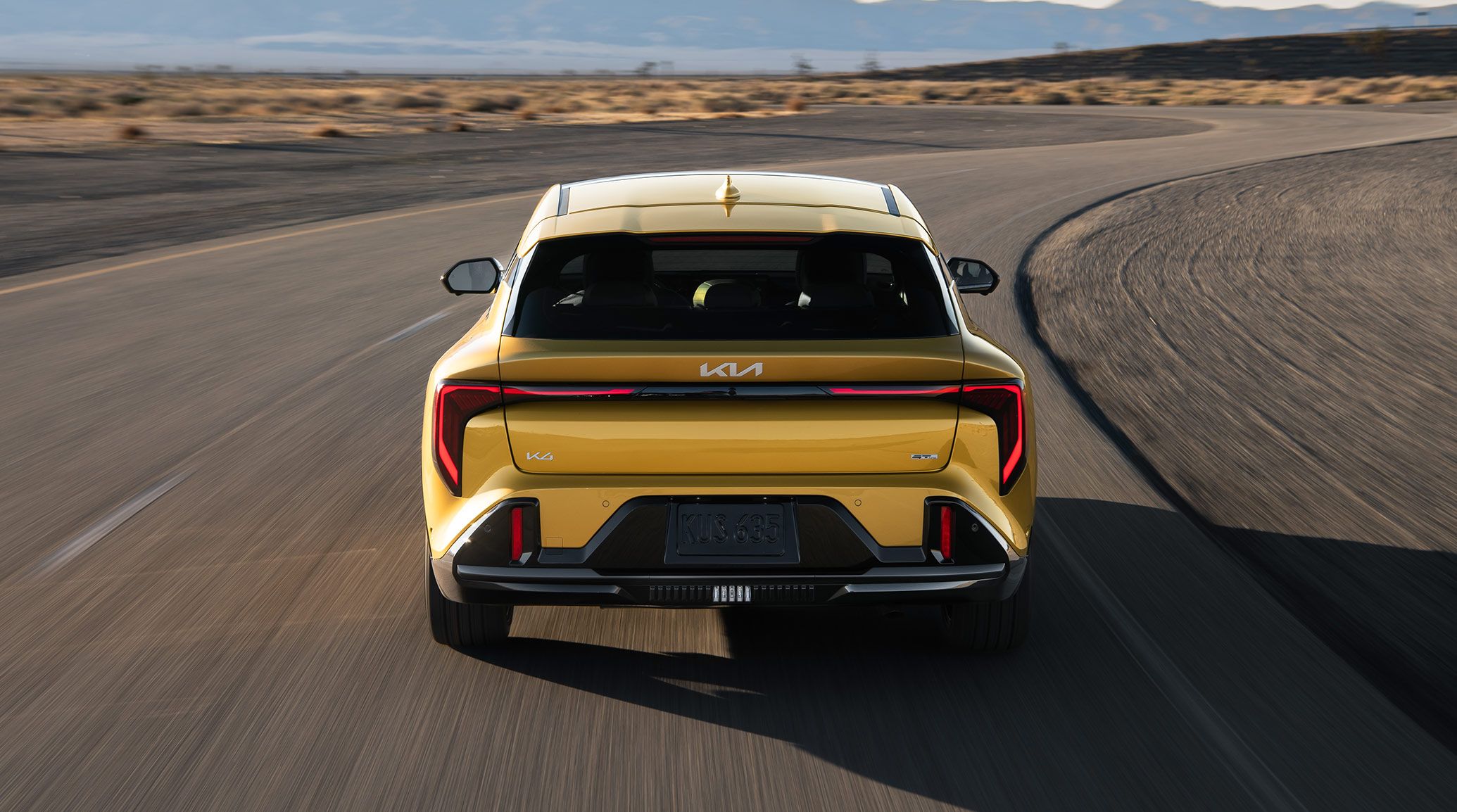 A Dynamic Exterior Shot of the 2026 K4 Hatchback GT-Line Turbo from the back to emphasize the Athletic Rear Bumpers while driving in the desert landscape.