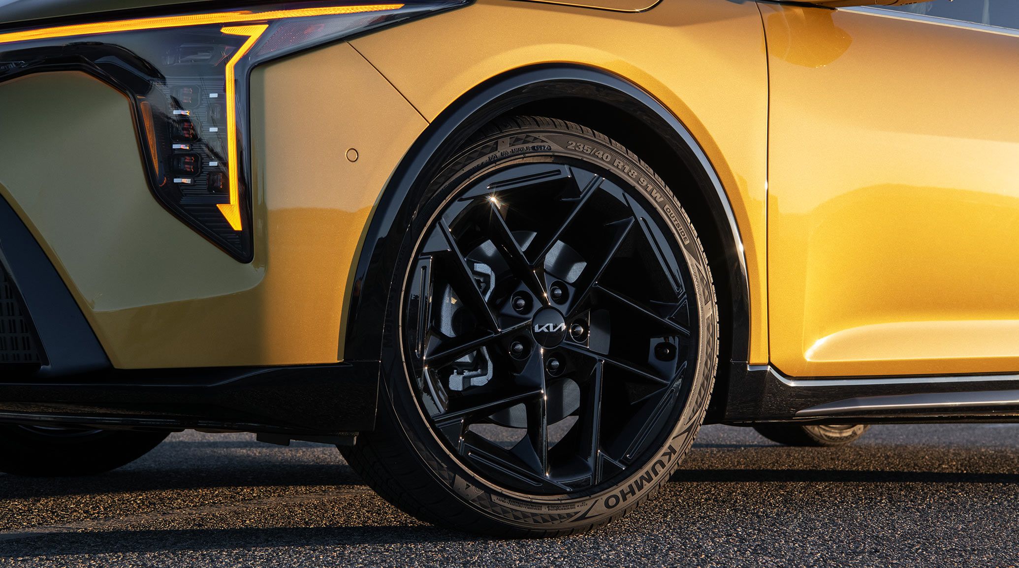 A standing exterior shot of the 2026 K4 Hatchback GT-Line Turbo in Gold Yellow; shot focuses on the 18-in. gloss black wheels that are on the GT-Line Turbo