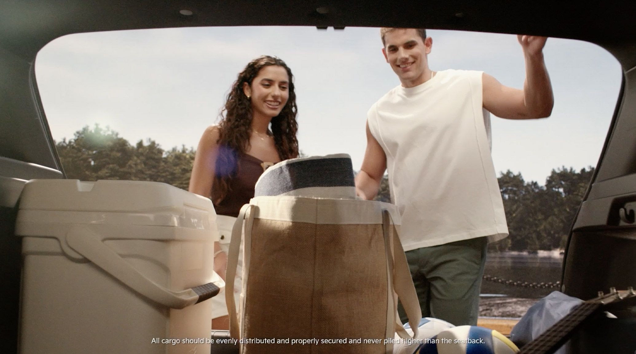 The 2026 Kia K4 Hatchback interior view of the cargo area with the rear hatch open. There is a couple loading belongings into the rear, highlighting the spacious rear storage and hatchback design.