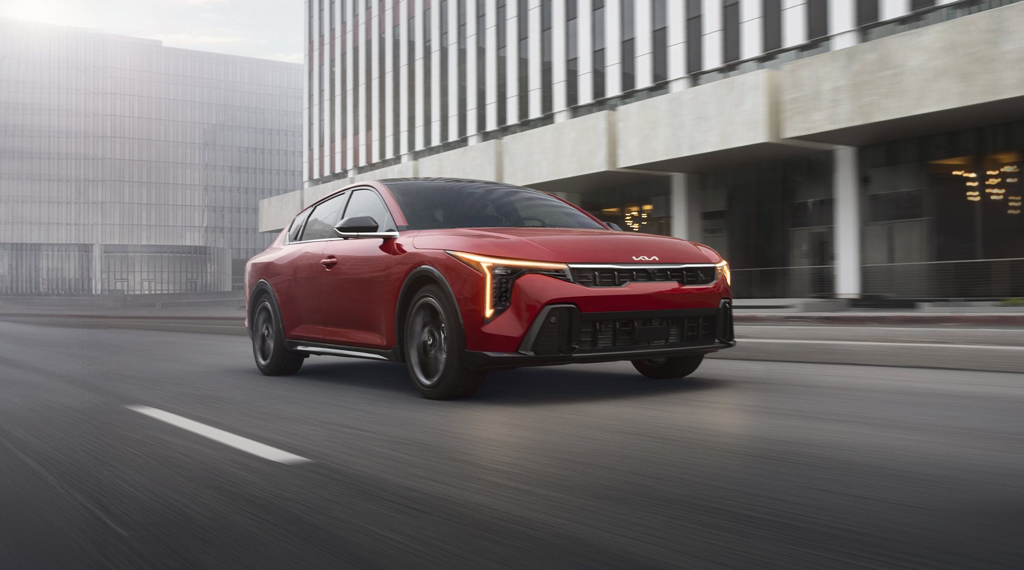 Dynamic shot of the 2026 Kia K4 sedan in red, looking stylish as it drives through an urban city environment