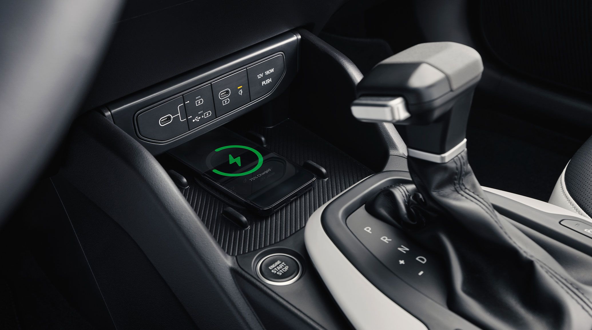 Close up of a cell phone charging in the forward center console of a Kia vehicle, also showing USB ports and the shifter