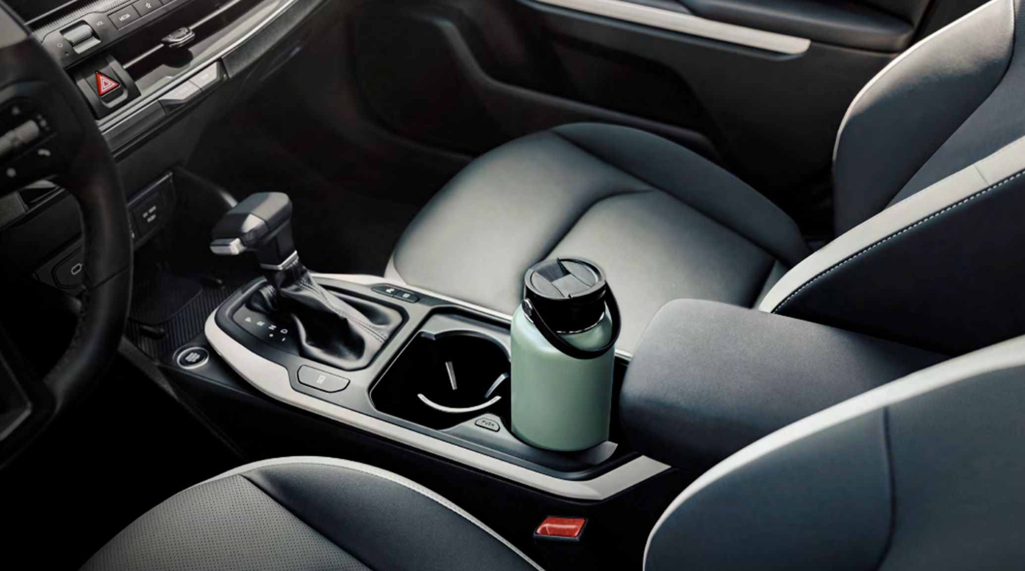 Interior view of the 2026 Kia K4 sedan's center console, including the shifter and large cupholders, one of which is currently holding a sizable light green water bottle