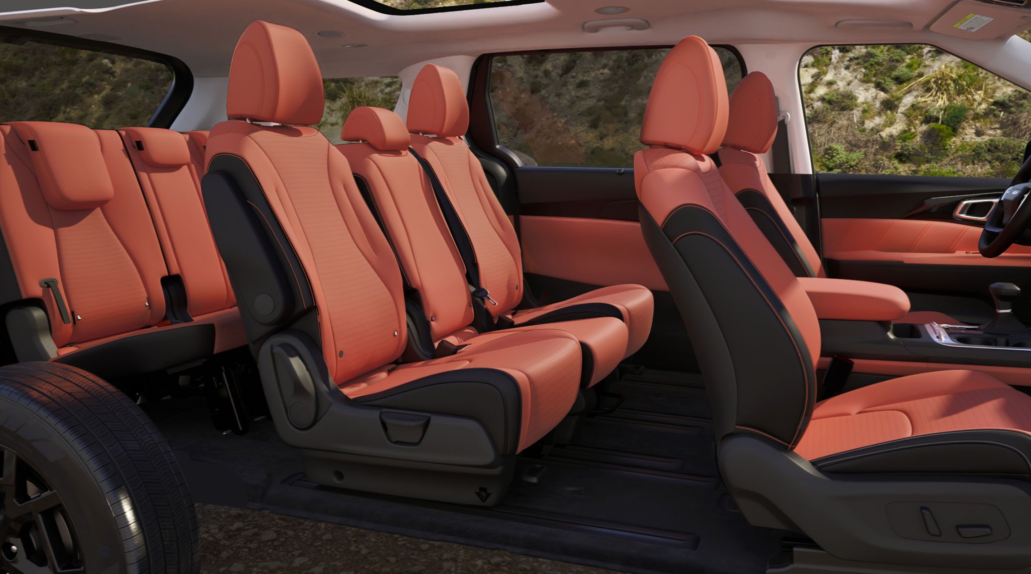 A side view of the 2027 Kia Carnival MPV highlighting its red-and-black three‑row seating interior. The image emphasizes the ample cargo space and premium 8-passenger seating, with rocky terrain and greenery visible through the windows.