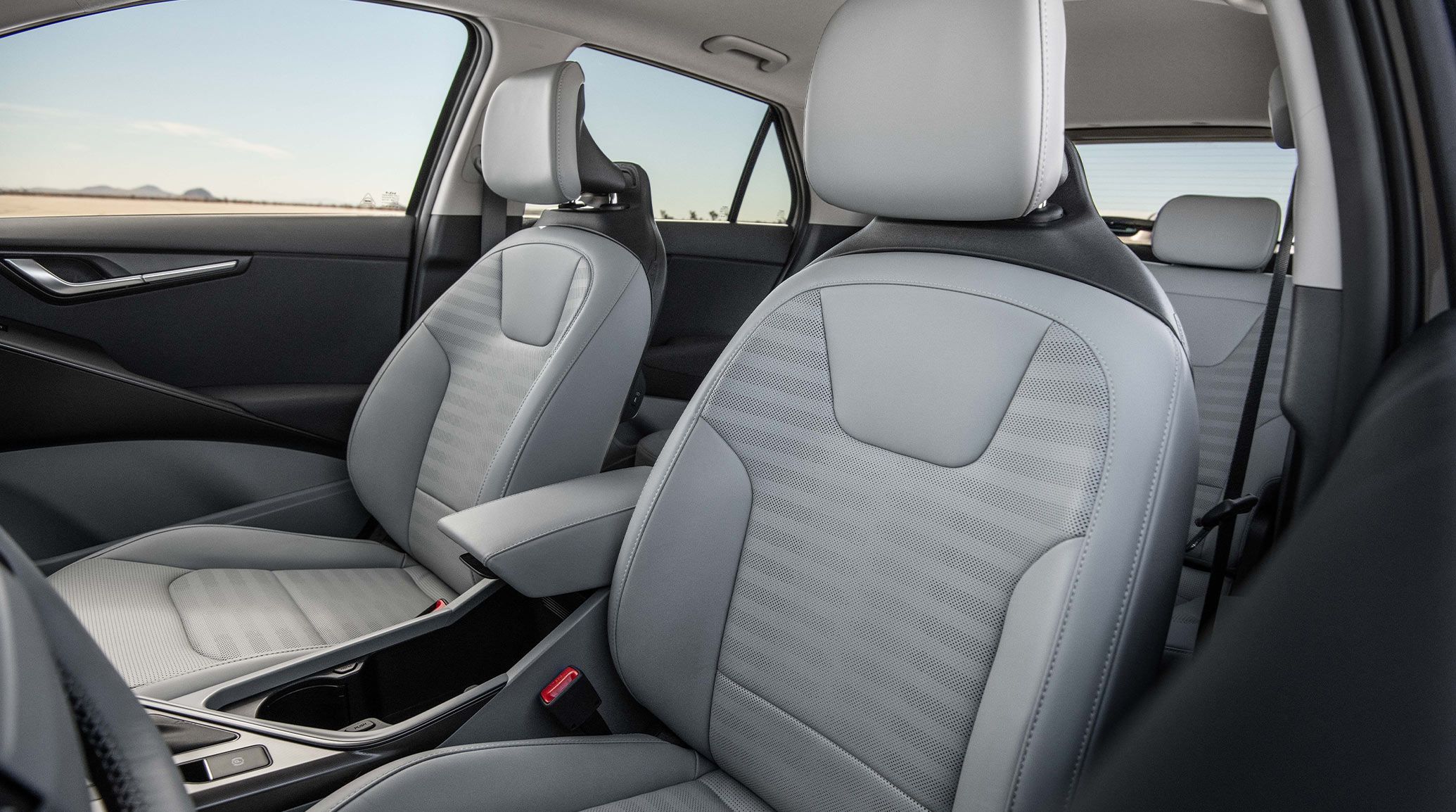 Interior view of the 2027 Kia Niro Hybrid Electric SUV focusing on the grey front driver and passenger seats, with a blue sky visible through the windows behind.