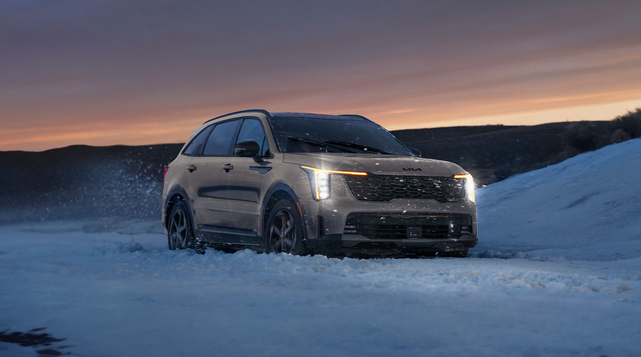 2026 Kia Sorento Plug-in Hybrid, three-quarter front view, with the headlights on driving through snow