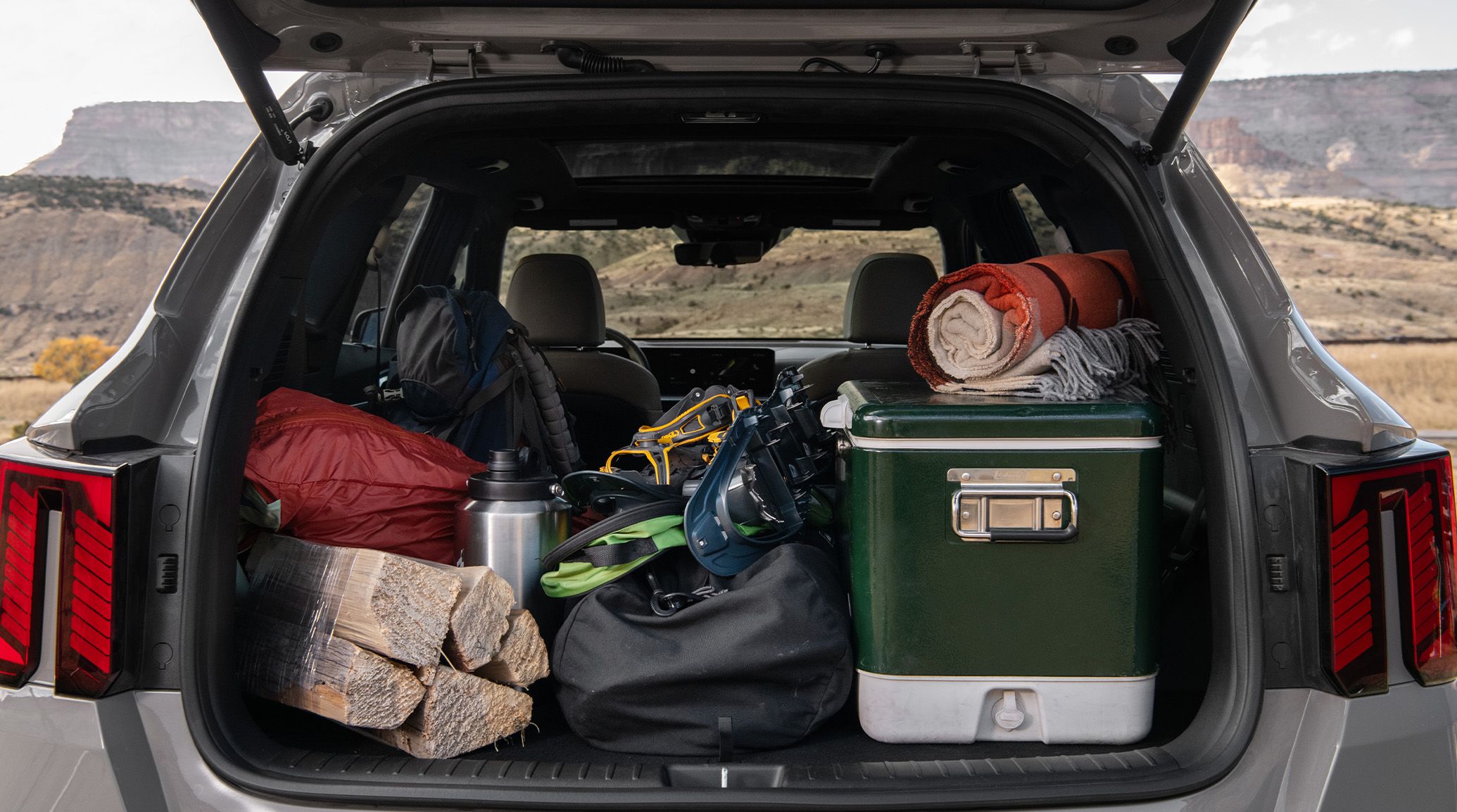 Close-up photo of the 2027 Kia Sorento with an open trunk showcasing the spacious cargo area packed with outdoor gear for camping, set against a hillside backdrop.
