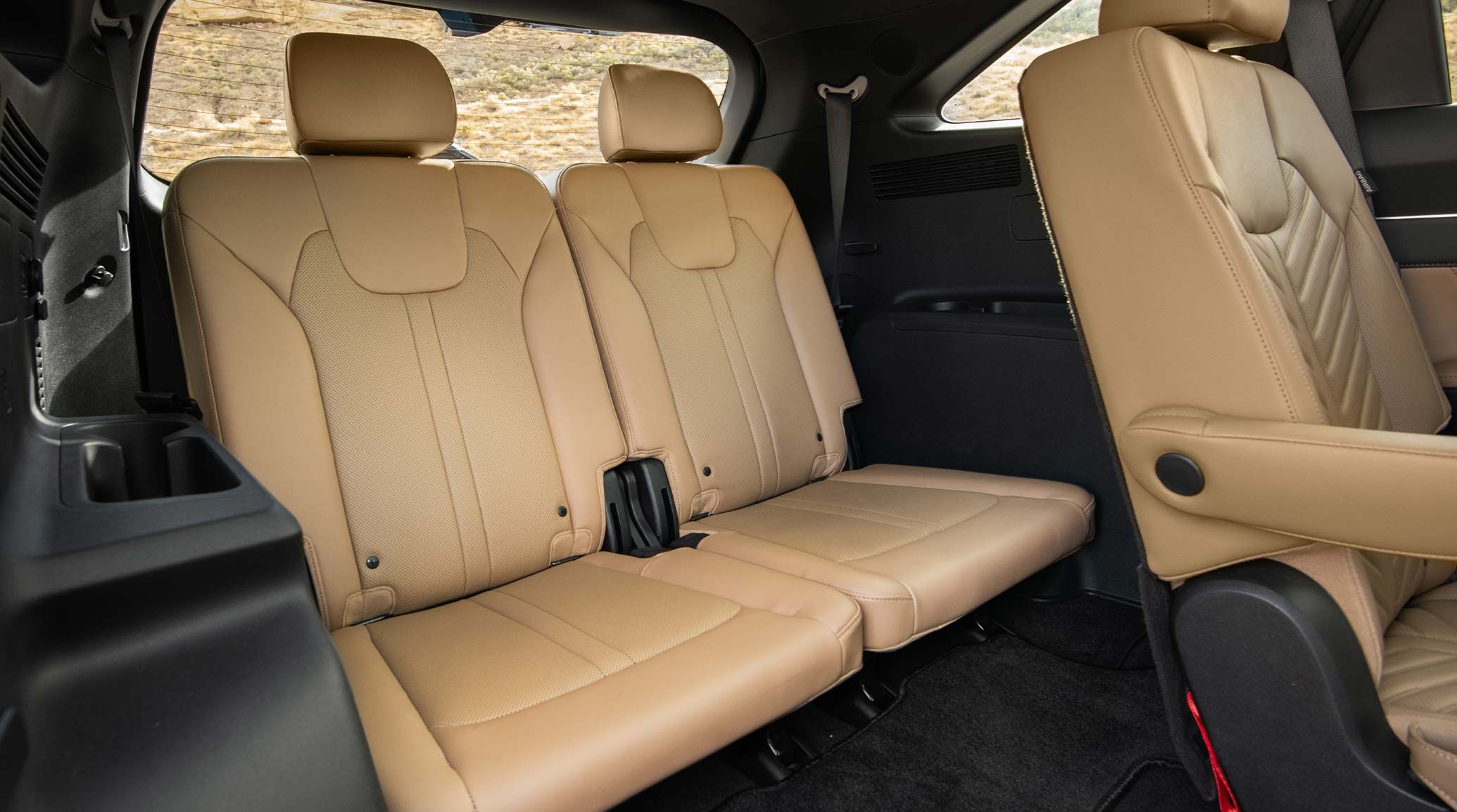 The 2027 Kia Sorento interior, featured in a three-quarter view of the spacious third-row seats in brown leather, with grass visible through the rearview mirror.