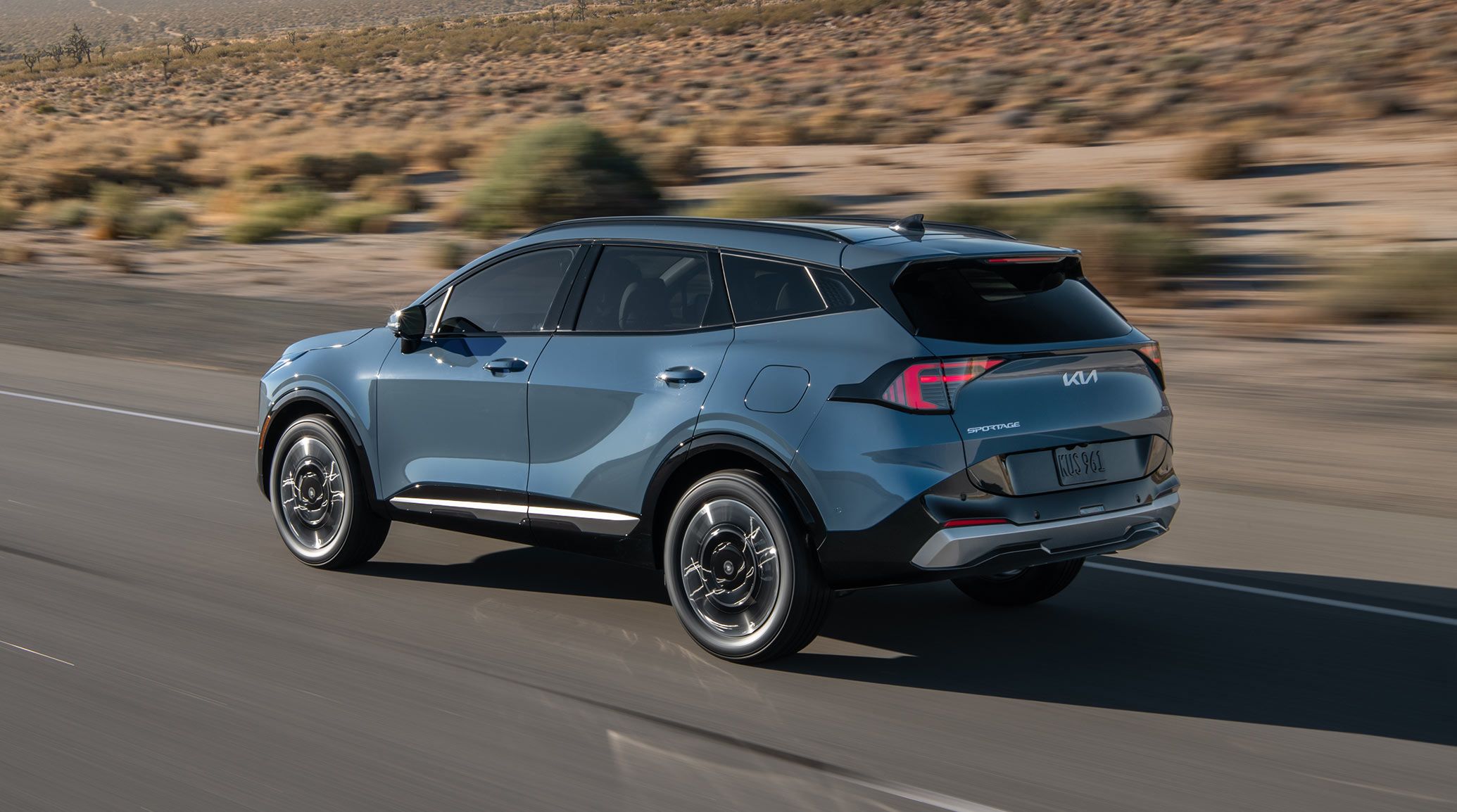 2027 Kia Sportage Hybrid Crossover SUV driving away on a desert road, shown in a rear three‑quarter view with its taillights and roofline visible.