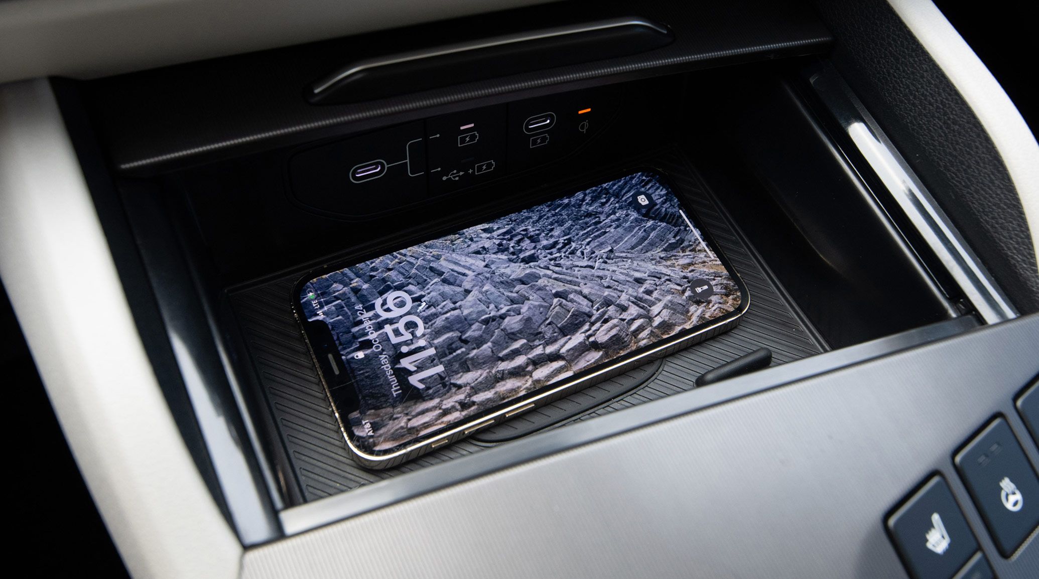 Close-up of the Kia interior wireless charging station with a smartphone halfway charged with a rocky landscape as the lock screen, highlighting advanced convenience and tech features.