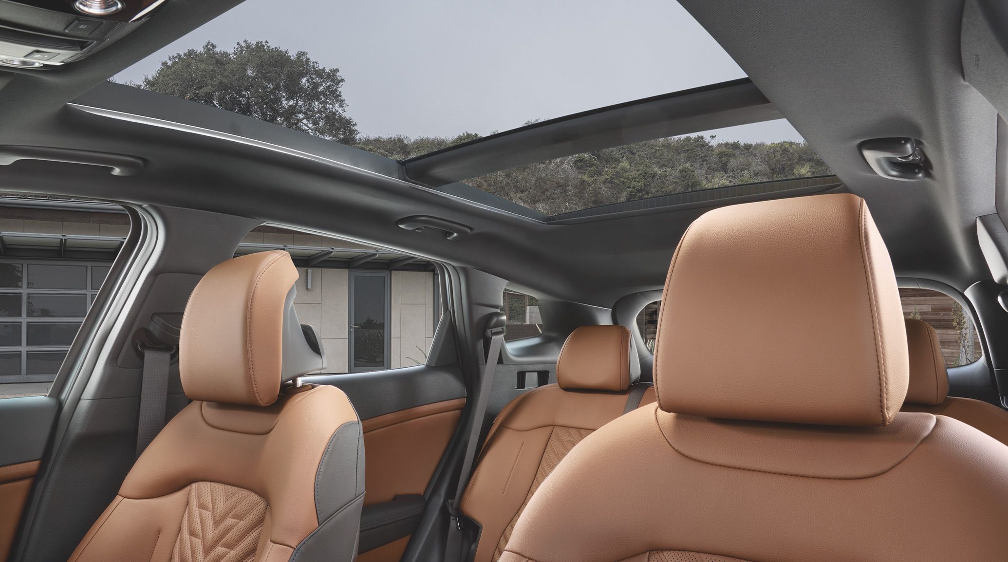 Interior view of the 2027 Kia Sportage Plug-In Hybrid, highlighting the available panoramic sunroof that gives an open driving experience. Blue skies and trees are visible through the sunroof.