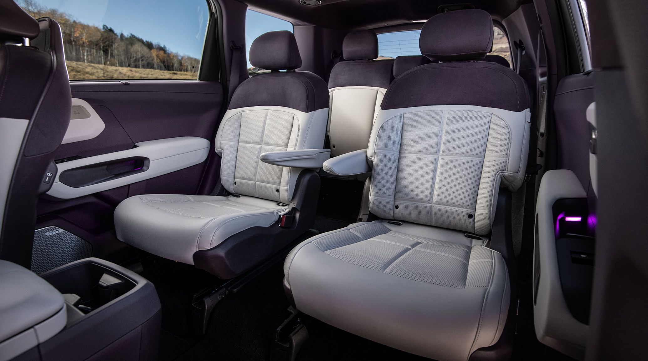 The 2027 Kia Telluride Hybrid second-row seats are highlighted in premium light gray and black, with adjustable armrests and spacious legroom, shown with panoramic side window view of the outdoors and modern cabin design.