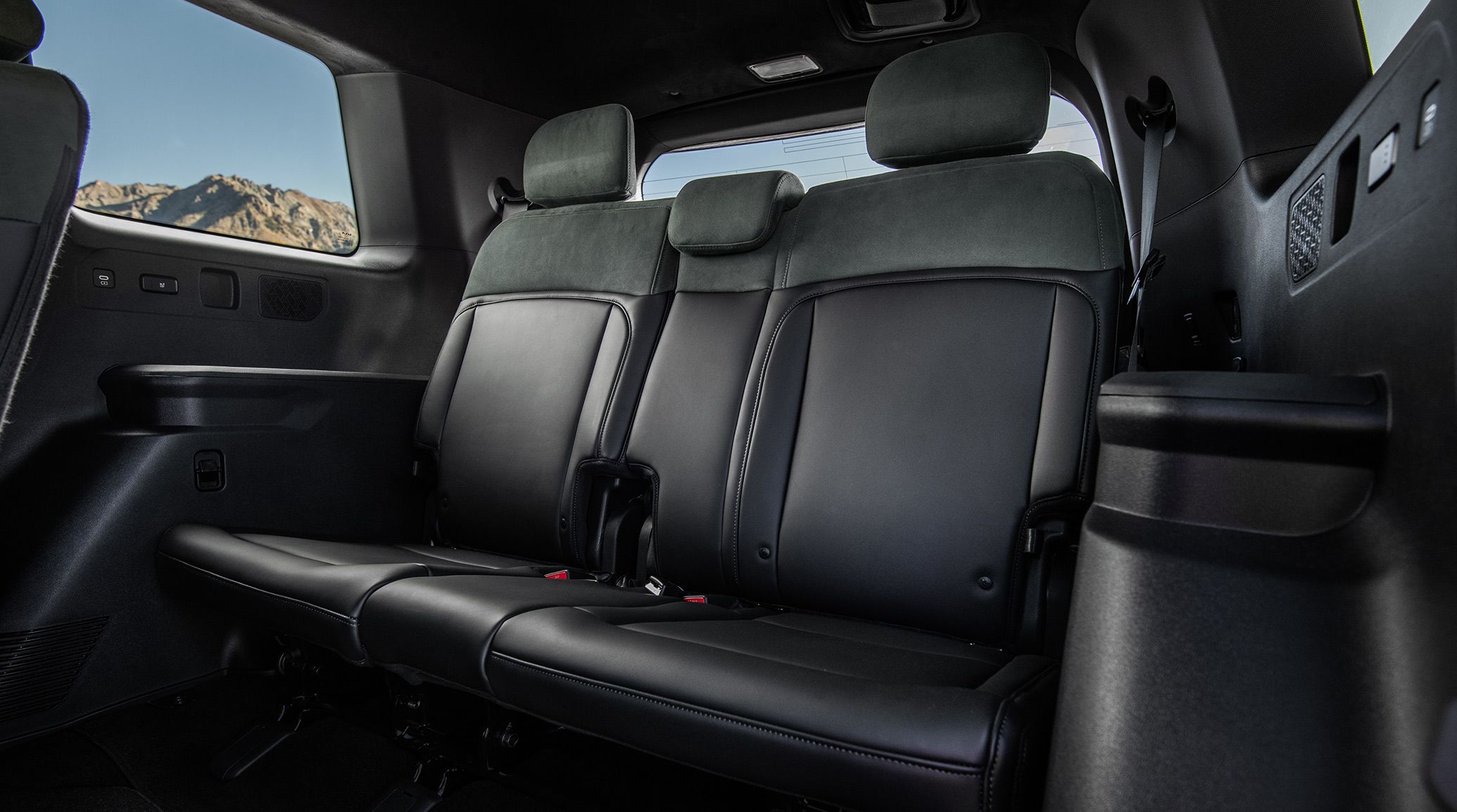 An interior view of the 2027 Kia Telluride Hybrid showcasing the black third-row seats and USB-C ports, with mountain peaks visible in the window to highlight the SUV's spacious design.