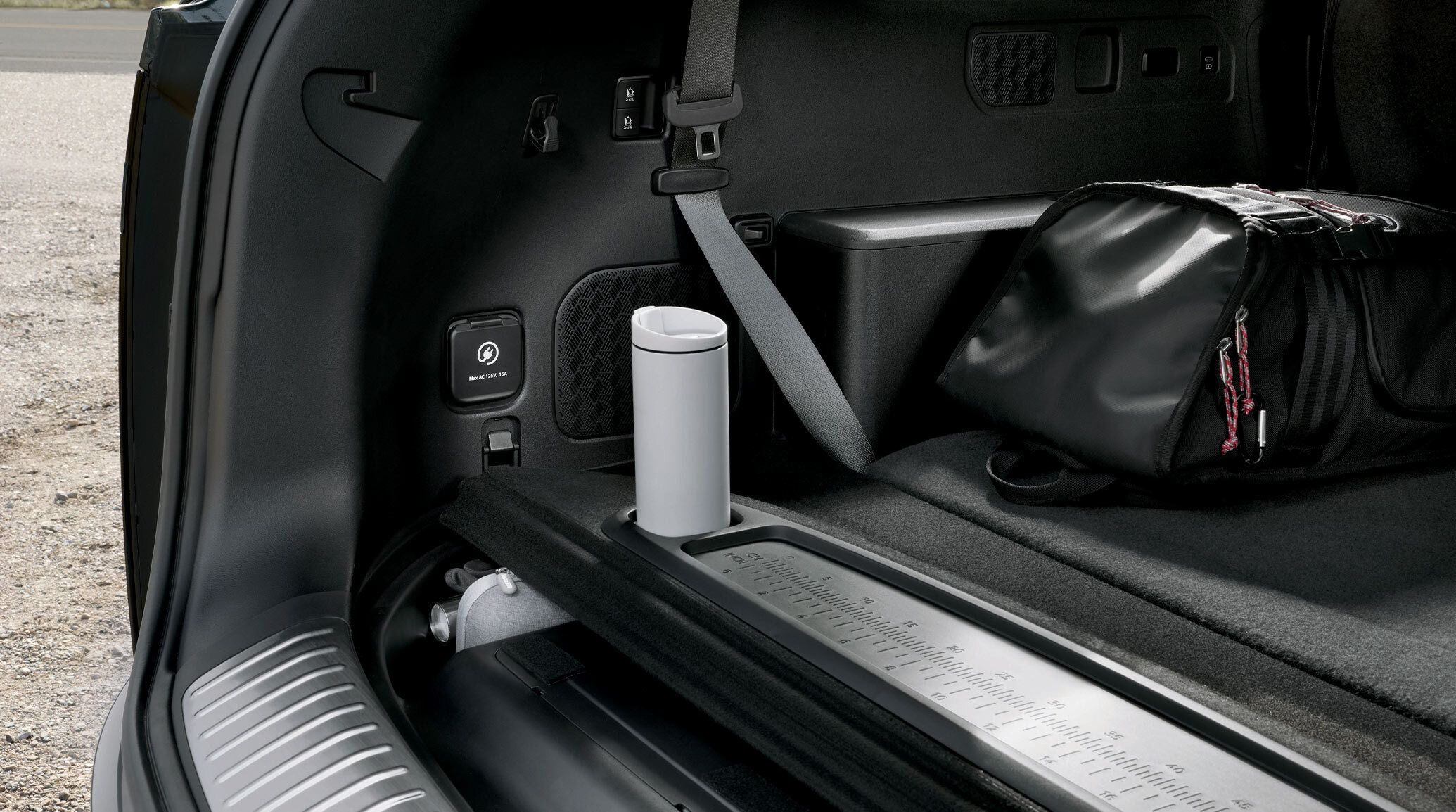 The back of the driver's seat in the 2027 Kia Telluride Hybrid SUV featuring the back pocket holding a cellphone that is plugged into an outlet in the seat, next to the center console and cupholders.