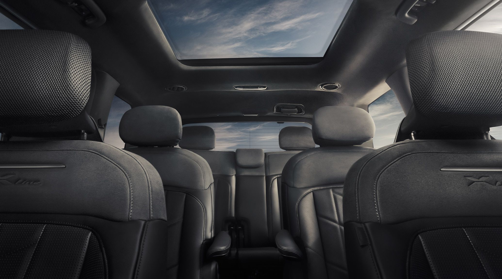 An interior image of the 2027 Kia Telluride Hybrid featuring black three-row seating, a wide sunroof, and comfortable headrests. Blue skies with clouds are peeking out through the windows and panoramic sunroof.
