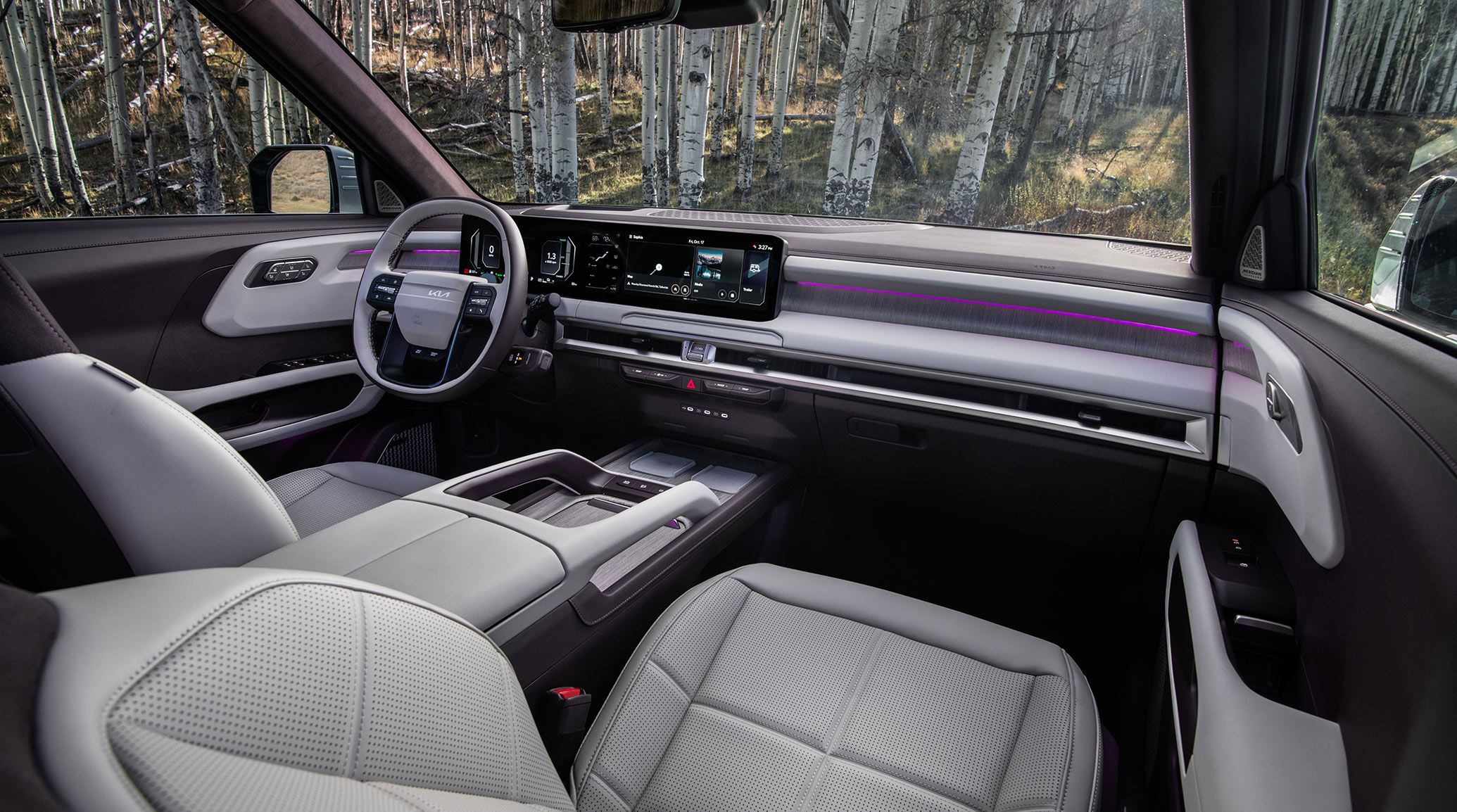 Interior view of the 2027 Kia Telluride Hybrid featuring a modern dashboard with a digital display, premium leather seats, a spacious center console, and ambient lighting, with tree visible through the windows.