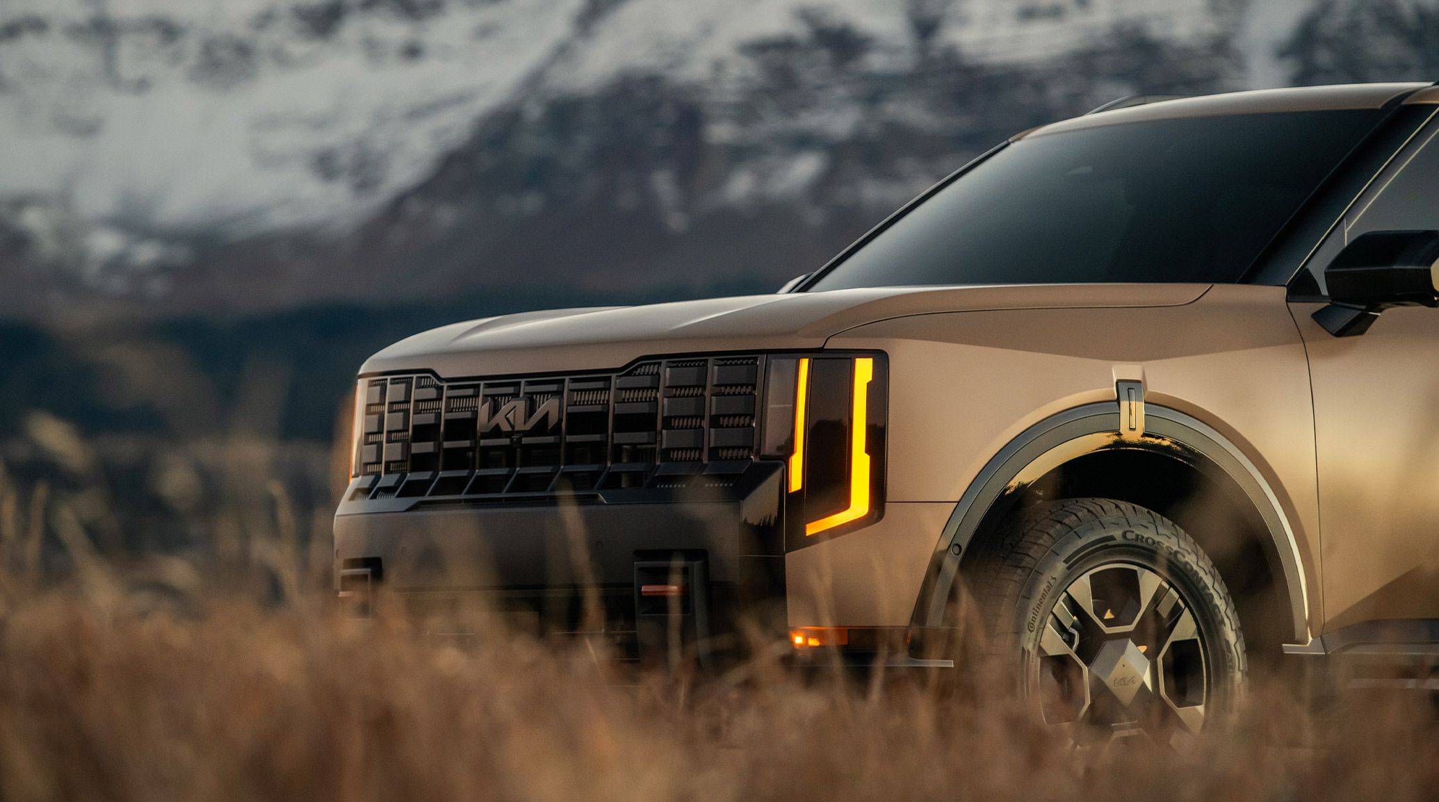 Close-up of 2027 Kia Telluride X-Pro SX Prestige in brown, showcasing bold front grille, gloss black surround, and signature vertical LED headlights, set against a rugged mountain backdrop.