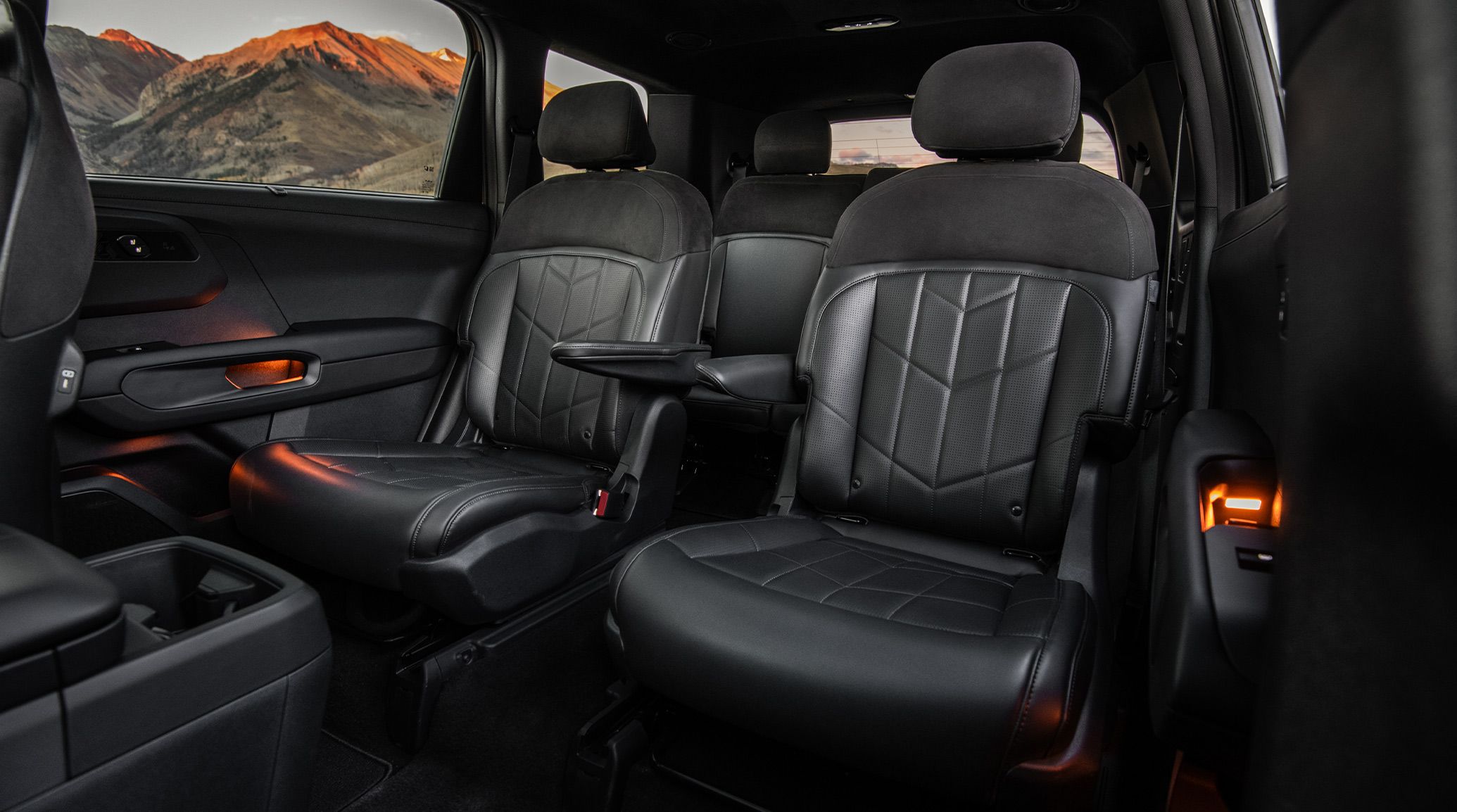 Interior shot of the 2027 Kia Telluride showcasing sleek black second-row seats highlighting the armrests, cupholders, storage space, and ambient lighting, framed by a scenic mountain visible through the windows.