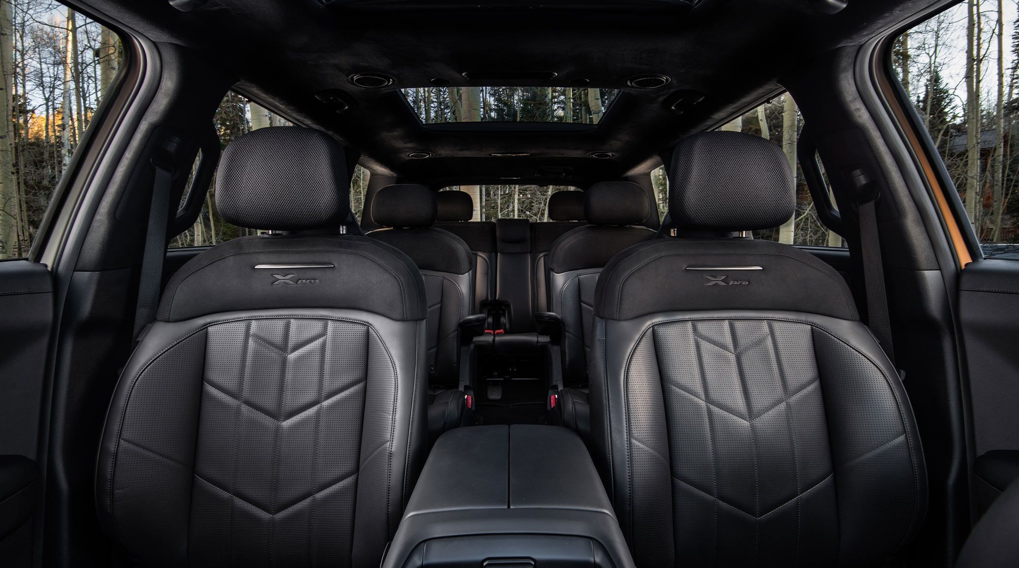 Interior view of the 2027 Kia Telluride X-Pro in black showcasing the 8-passenger seating layout with premium leather chairs. Forest views are peaking out of the windows and sunroof highlighting the SUV's spacious design.