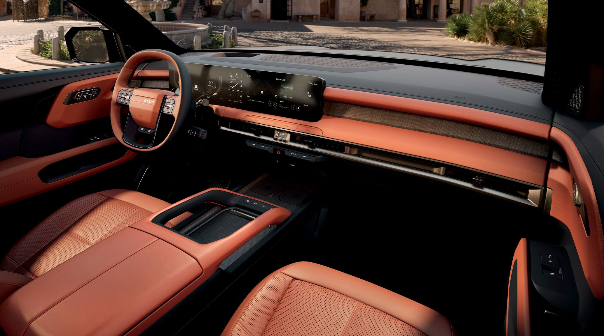 Interior view of the 2027 Kia Telluride featuring a red and navy interior with the driver-side steering wheel, digital display, and center console highlighted, with a house’s driveway visible through the windshield and window.
